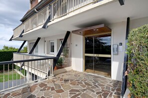 Ein zweistöckiges Gebäude mit einer einbruchhemmenden Eingangstür aus Steinplatten, einem Balkon mit Metallgeländern und einer Holzbalkendecke.