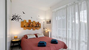 Et soveværelse med seng, puder, et natbord, en lampe, en radiator og et vindue med gardiner.