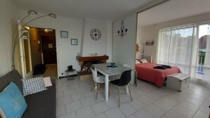 Ein moderner, hell erleuchteter Raum mit einem Bett, einem Esstisch mit Stühlen, einer Couch und einer kleinen Küchenzeile.