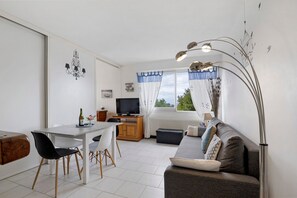 Un espace de vie compact comprenant un coin repas, un canapé, un téléviseur et une fenêtre avec des rideaux.