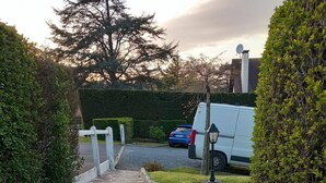 Ein Steinweg führt zu einem Parkplatz, in dessen Nähe ein weißer Transporter steht.