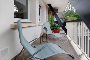 Un balcon avec deux chaises, une petite table et un pot de fleurs.