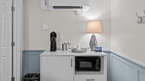 Een kitchenette met een koffiezetapparaat, magnetron en een kleine tafel met een lamp en een boek.