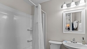 Een badkamer met douchegordijn, toilet, wastafel en spiegel.