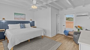 Ein Schlafzimmer mit Bett, Nachttischen, Deckenventilator, Fenster mit Jalousien und Klimaanlage.
