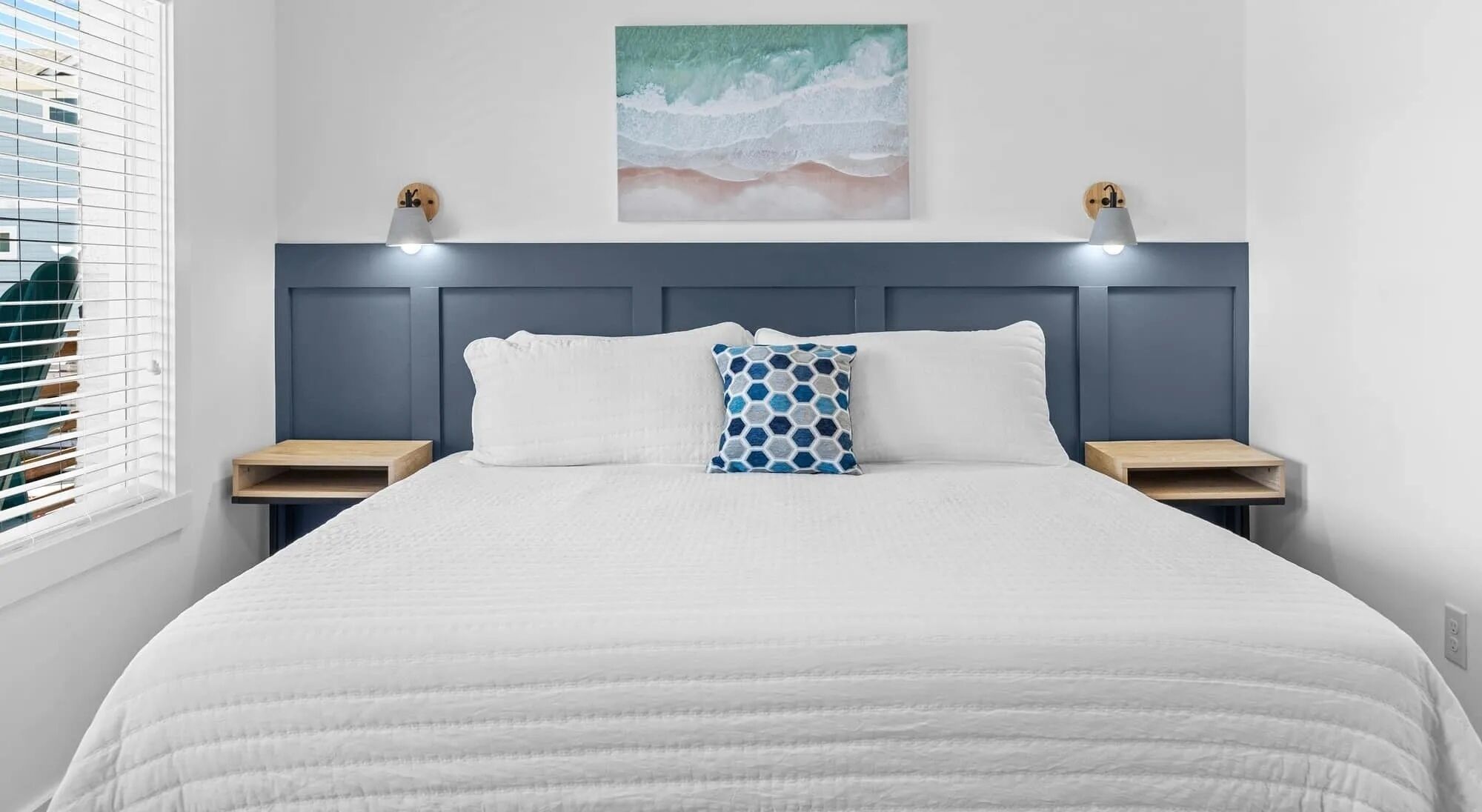 A neatly made bed with a white quilt, two bedside tables, and a wall-mounted light fixture.