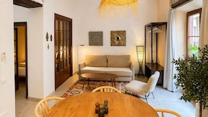 A cozy living room with a wooden dining table, a sofa, and a hanging light fixture. - Prado Suites Apartments (Málaga)