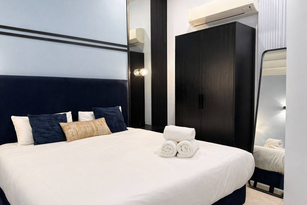 Ein modernes Hotelzimmer mit einem großen Bett, einem dunklen Kopfteil und einem Kleiderschrank.
