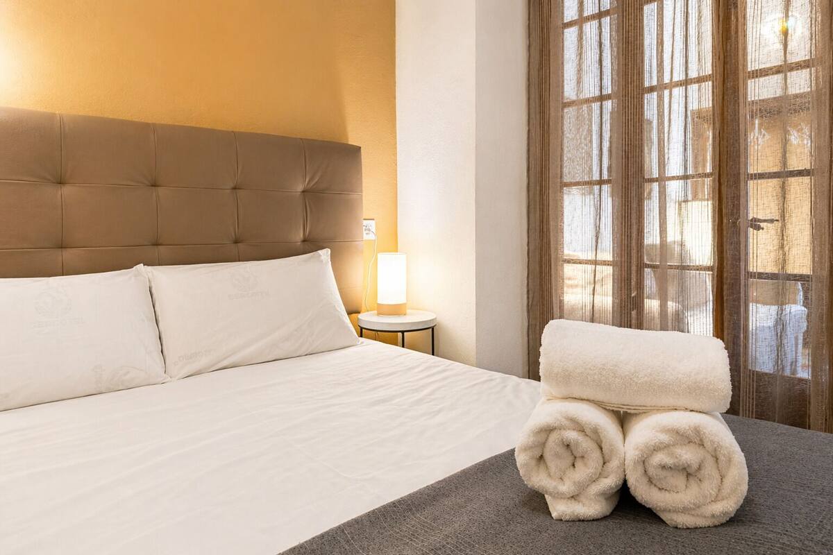 Ein Hotelzimmer mit einem großen Bett, einer Nachttischlampe und einem Fenster mit Vorhängen.
