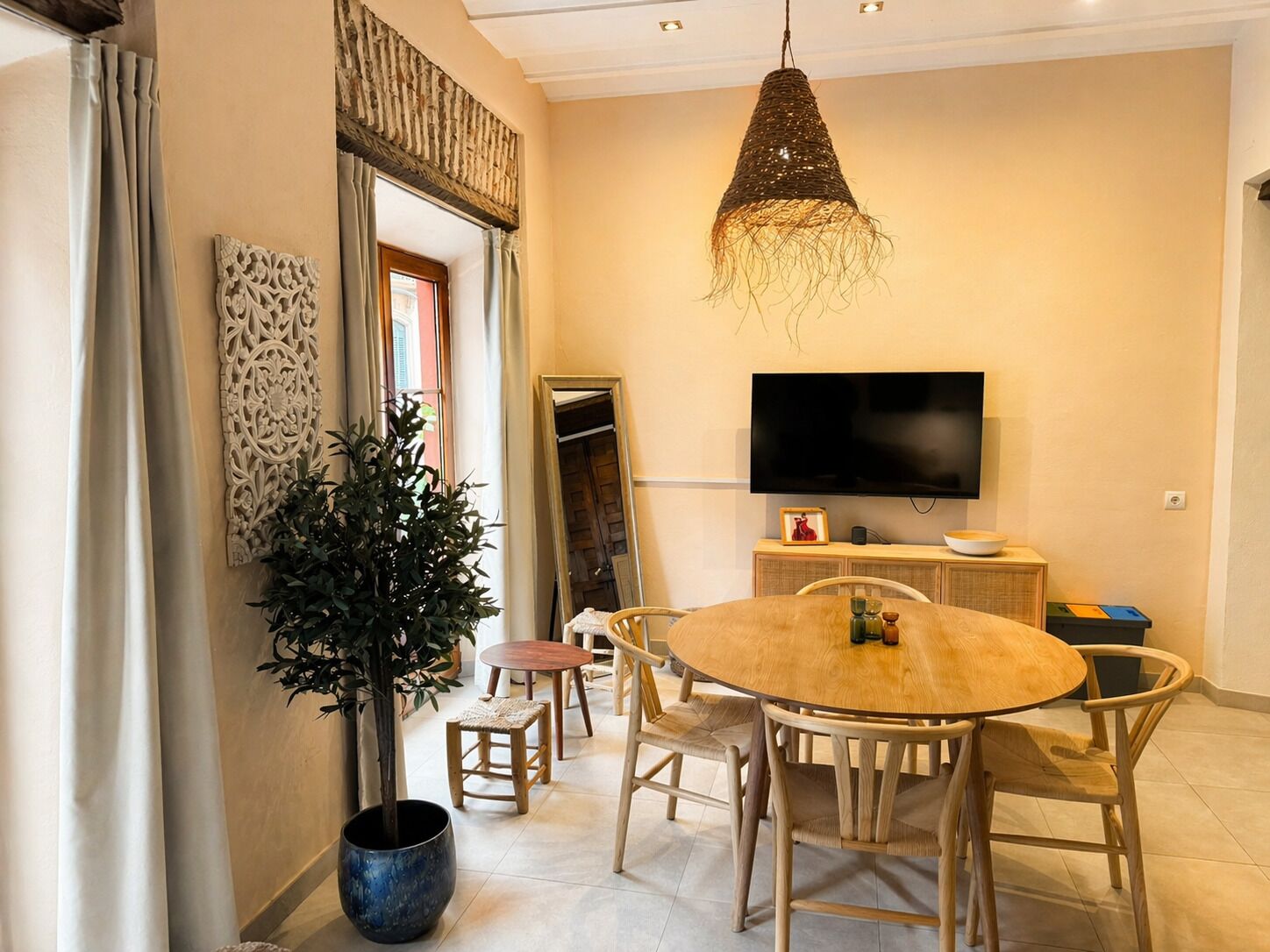 A dining area with a round table, chairs, a potted plant, a television, and a decorative wall piece.