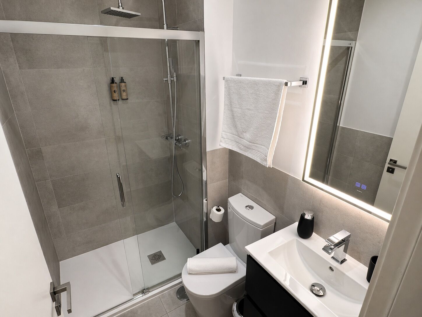 Une salle de bain moderne avec une douche à parois de verre, des toilettes, un lavabo avec un miroir et un porte-serviettes.