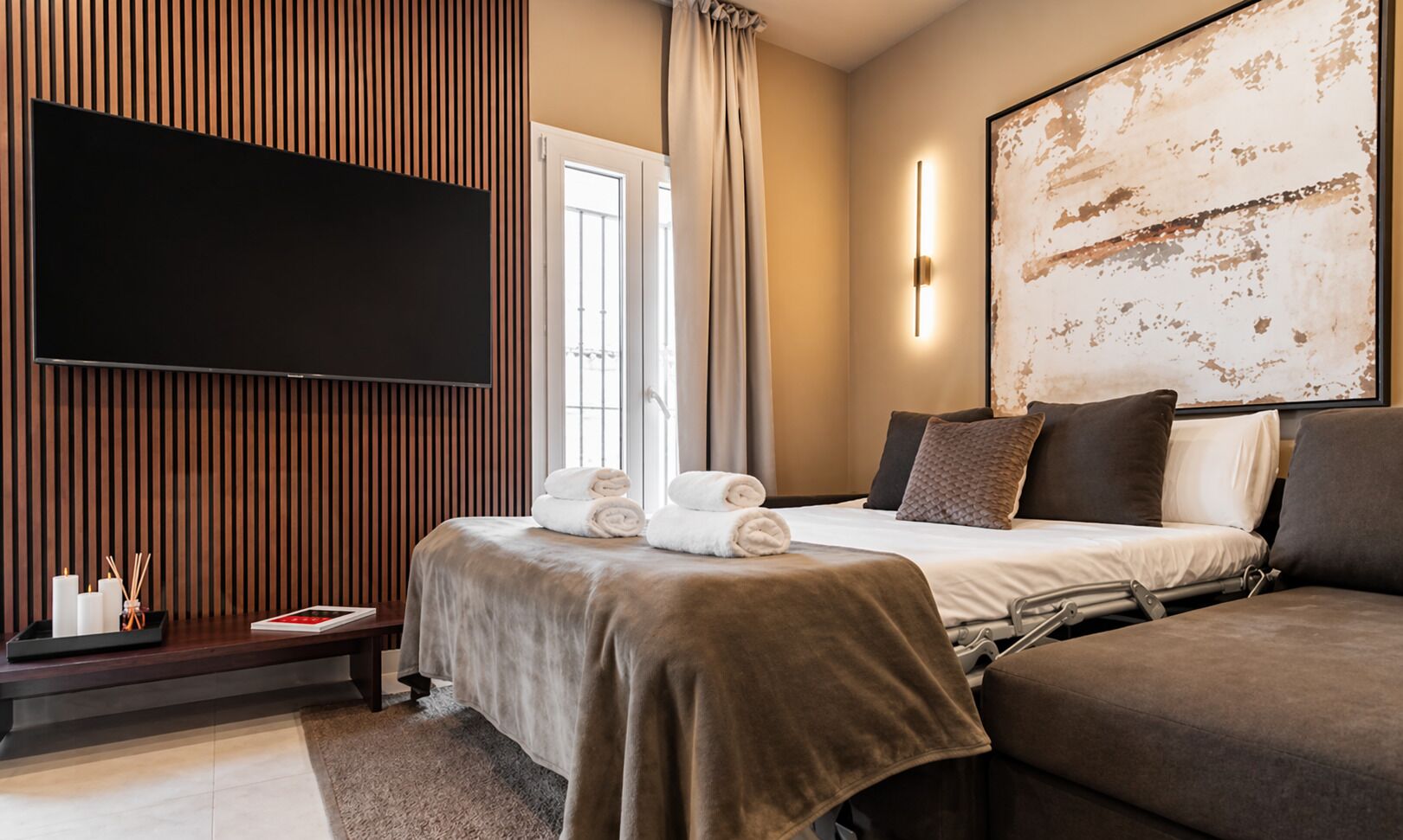 Habitación de hotel moderna con una cama grande, un televisor de pantalla plana, un cuadro abstracto de gran tamaño y vistas al exterior.