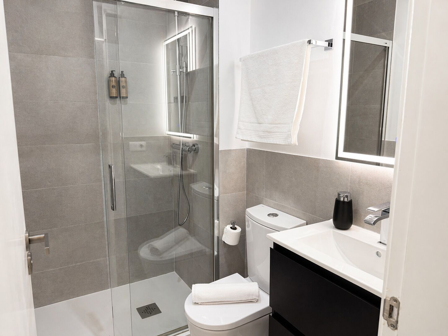 Une salle de bain moderne avec une douche à parois de verre, des toilettes blanches, un lavabo avec un miroir et un porte-serviettes.