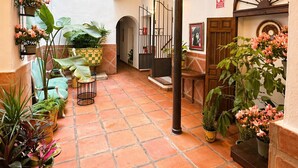 A courtyard with tiled flooring, potted plants, a staircase, and a door with a decorative arch. - Prado Suites Apartments (Málaga)