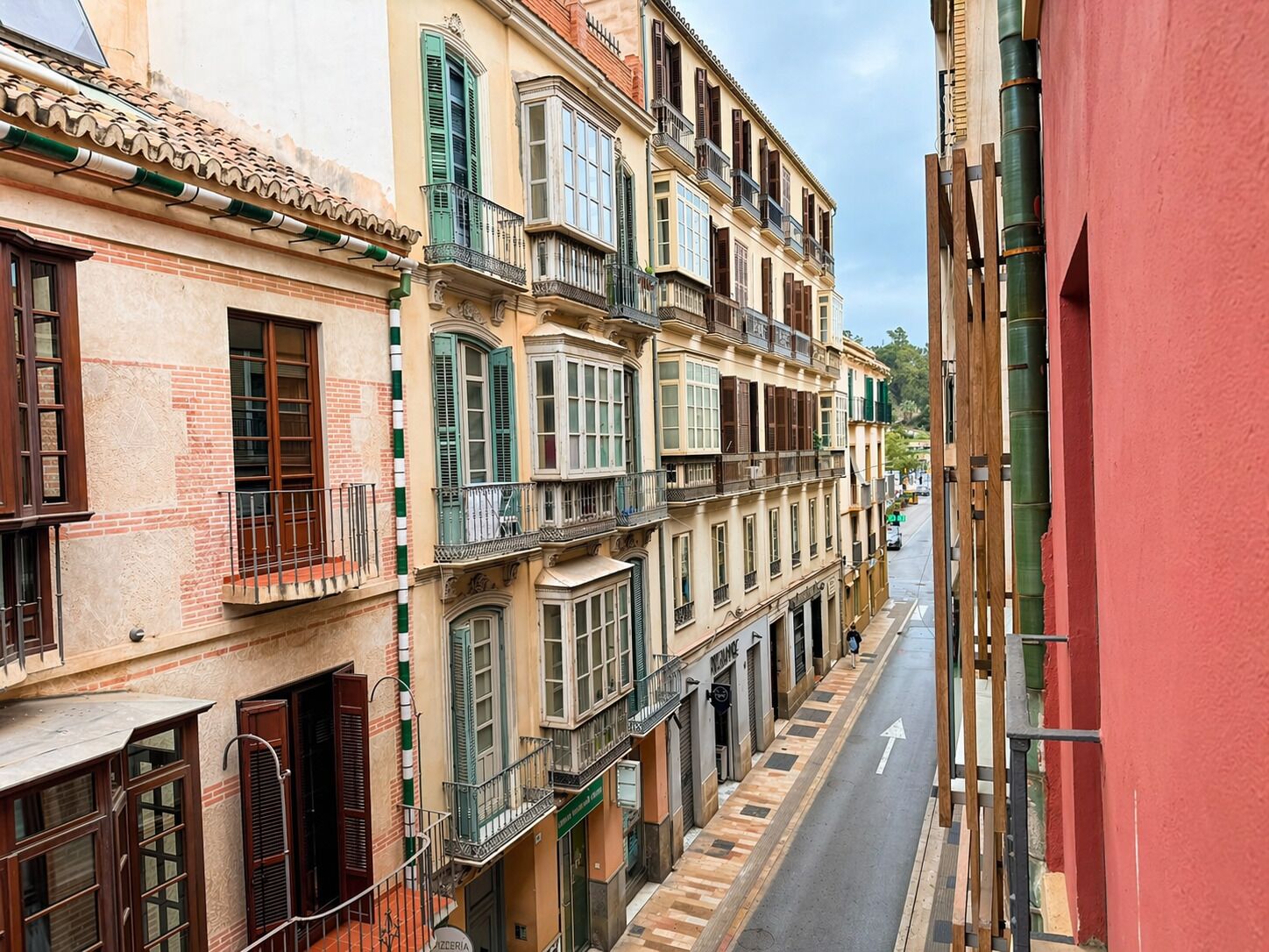 A narrow street with multi-story buildings, balconies, and a clear sky.