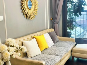 A sofa with a tufted backrest, a cushion with a yellow pillow, and a grey blanket.