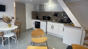 Uma cozinha moderna com armários brancos, micro-ondas e pia. Há uma área de refeições com mesa e cadeiras, e uma escada que leva a um andar superior.