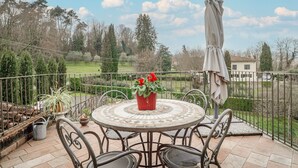 Un patio con una mesa redonda y sillas, una planta en maceta y una estatua.