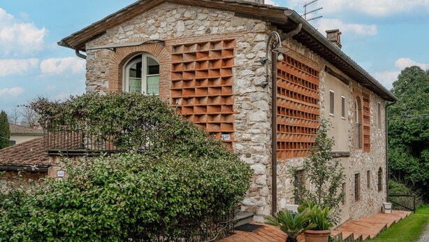 Una casa de piedra con techo de tejas, chimenea y un pequeño balcón.