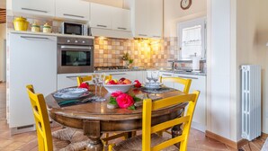 Una cocina con armarios blancos, estufa, microondas y una mesa de comedor con sillas.