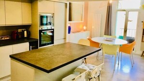 A modern kitchen with a central island, built-in appliances, and a dining area with a round table and chairs. - "Zarago 3" T3 Design in Duplex, Clim & Wifi (Sète)