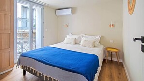 Ein Schlafzimmer mit einem Bett, einem kleinen Hocker, einer Wand-Klimaanlage und einer Balkontür.