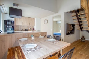 Una cocina moderna con armarios de madera, horno integrado y un comedor con una mesa grande dispuesta para cuatro.