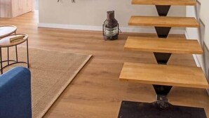 Eine moderne Treppe mit Holzbeschlägen und schwarzen Metallstützen, die zu einer zweiten Etage führt. Eine flache Bildschirmfernseher ist an der Wand oberhalb der Treppe angebracht.