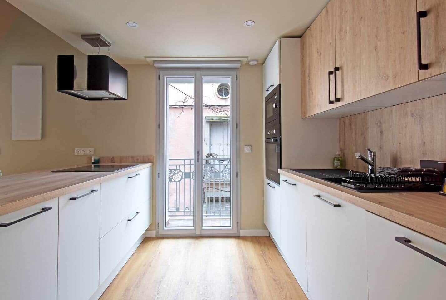 Una cocina moderna con armarios blancos, encimera de madera y puerta corredera de vidrio que da a un balcón.