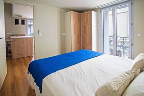 Un dormitorio con una cama, una manta azul, armario de madera y un balcón con barandilla de metal.