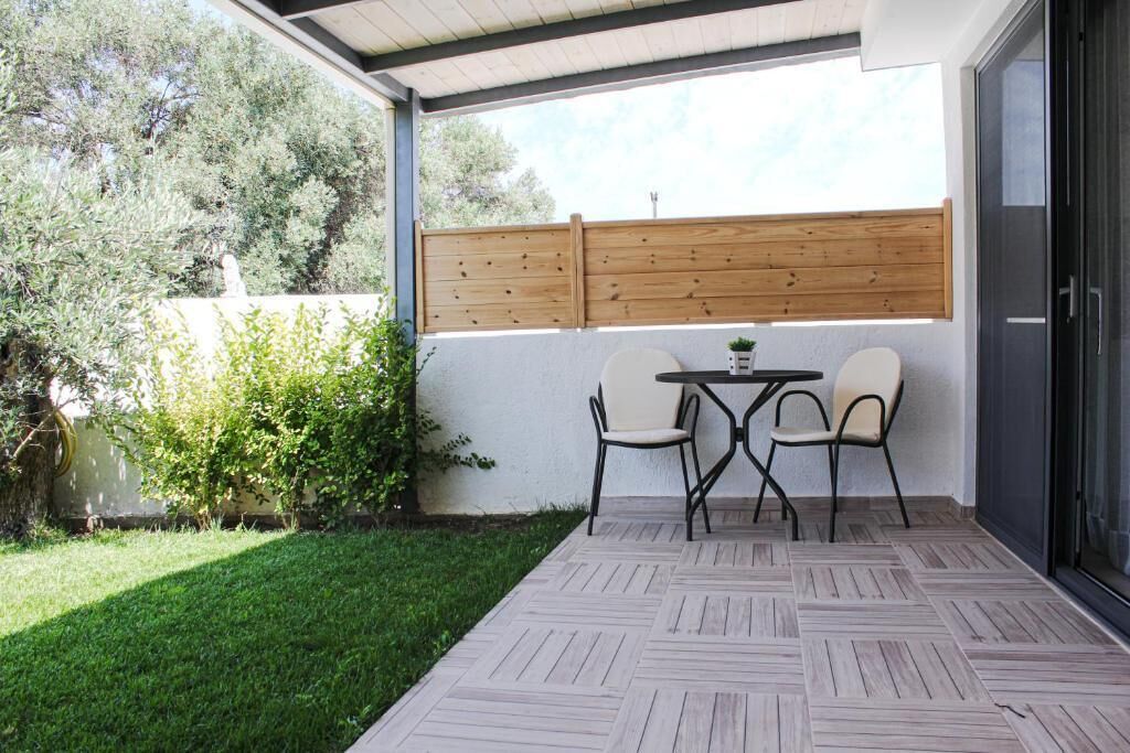 A covered patio with a herringbone-patterned floor, two chairs, a small table, and a wooden fence.