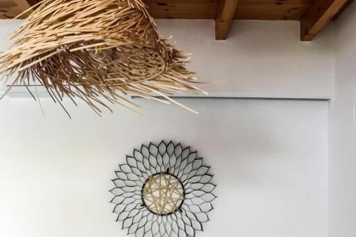 Une chambre moderne avec un lit gris, un élément décoratif mural et un luminaire suspendu au plafond, fait de fibres tressées.