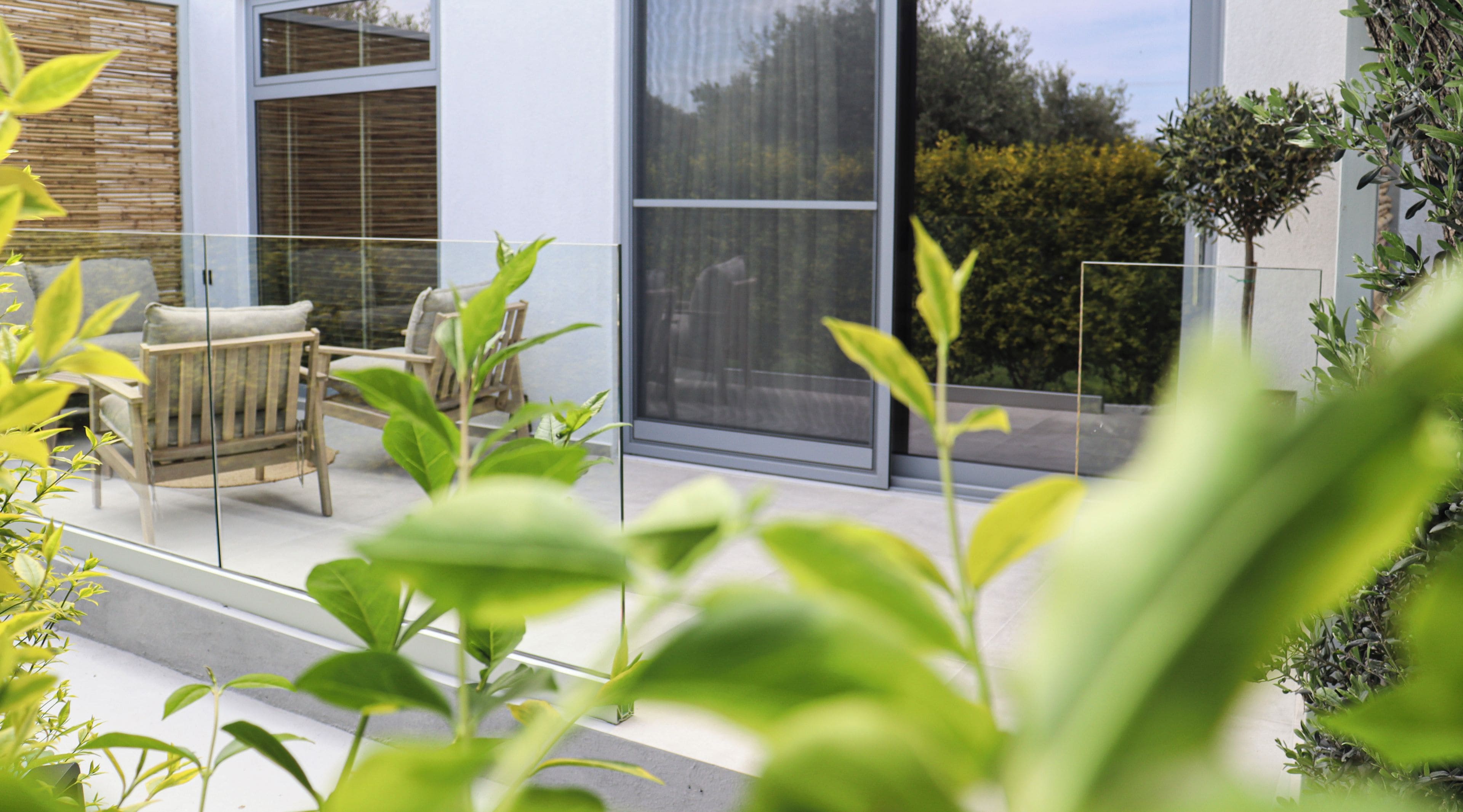 Un espace extérieur moderne, aménagé avec une balustrade en verre, un banc en bois et des plantes en pot.