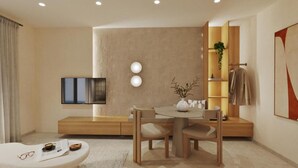 Una habitación de hotel moderna con diseño minimalista, que incluye un televisor de pantalla plana, una mesa redonda con sillas, un sofá y un banco empotrado con una planta.