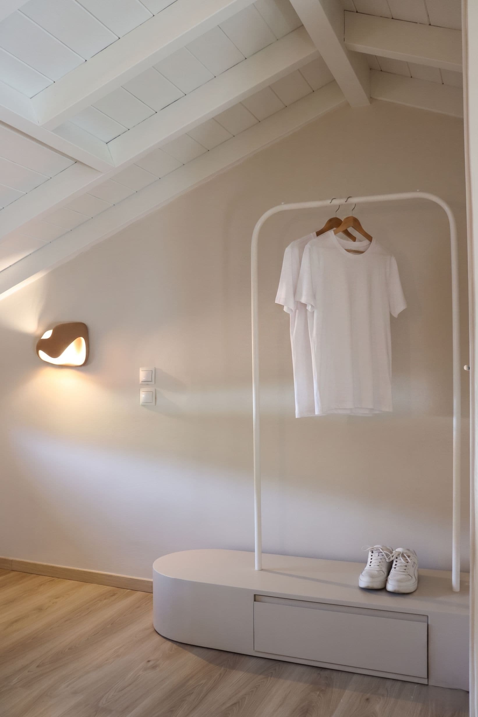 Una habitación minimalista con un armario blanco, un zapatero colgante y una lámpara fijada a la pared.