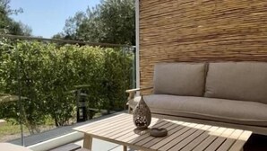 Un espacio al aire libre con mesa y banco de madera, un sofá color crema y un jarrón decorativo.