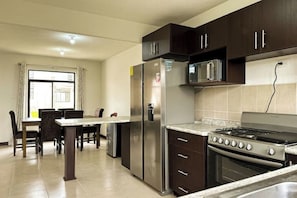 A kitchen with dark cabinets, stainless steel appliances, a dining area with a table and chairs, and a window with curtains.