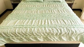 Un lit recouvert d’une couverture verte à motifs et agrémenté d’oreillers assortis, avec deux tables de chevet de chaque côté.