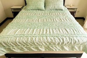 Un lit recouvert d’une couverture verte à motifs et agrémenté d’oreillers assortis, avec deux tables de chevet de chaque côté.