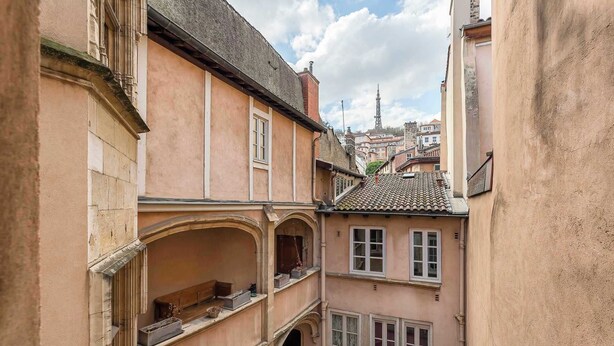 A narrow street with buildings featuring traditional architecture, including a balcony with a railing and a window with a decorative grille. - Neyret - Furnished apartment - Downtown Lyon (Lyon)