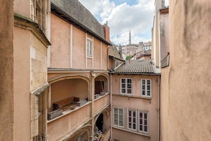 A narrow street with buildings featuring traditional architecture, including a balcony with a railing and a window with a decorative grille.