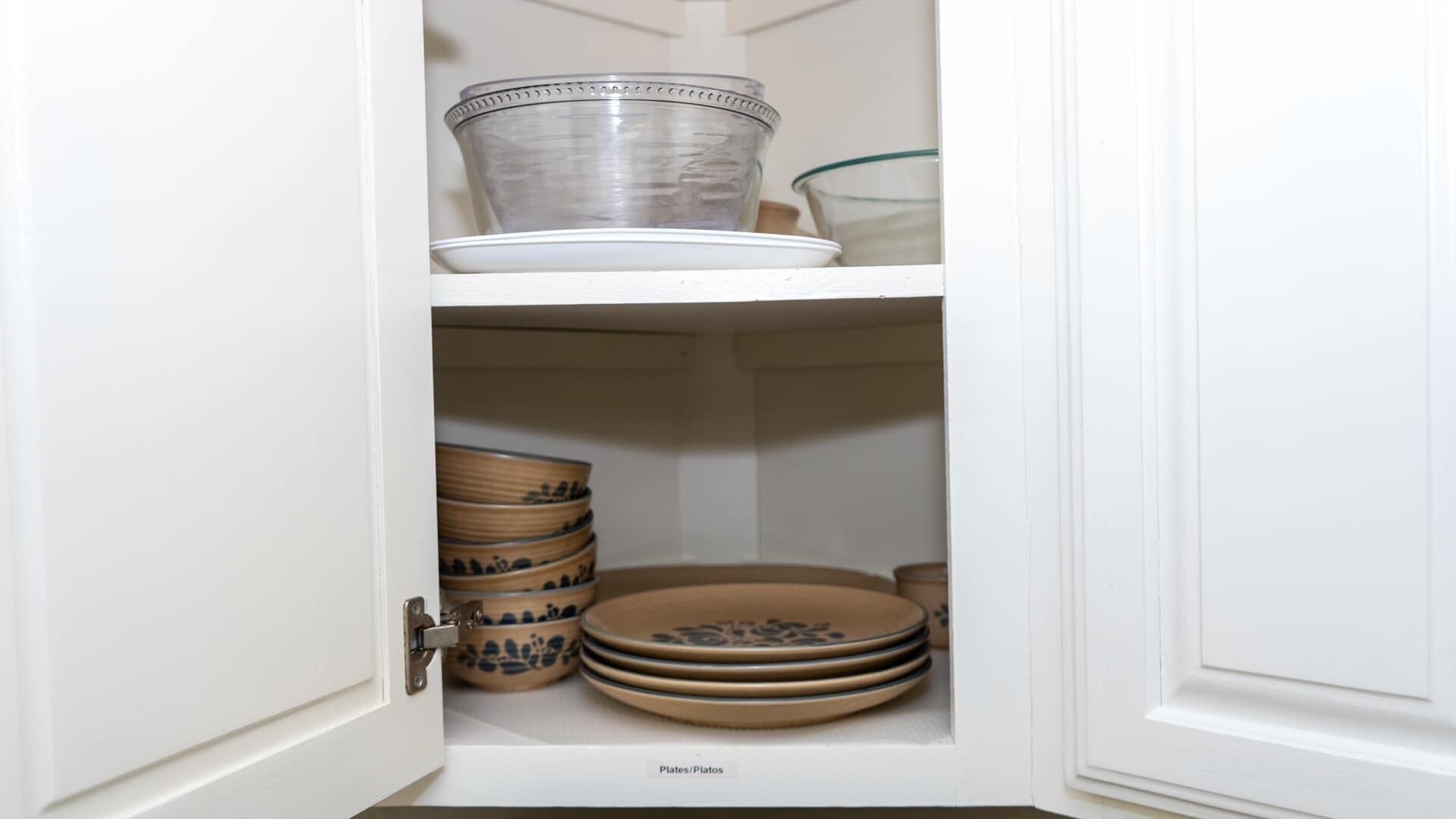 A cabinet with shelves containing plates, bowls, and a glass container.