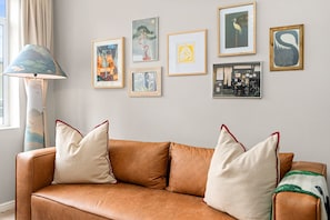 A brown leather sofa with white and red pillows, a floor lamp, and several framed artworks on the wall. - Fairmont 22 on Hof (Cape Town)