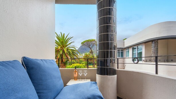 Un balcone con un divano blu, un'alta colonna cilindrica e vista su montagne e vegetazione.