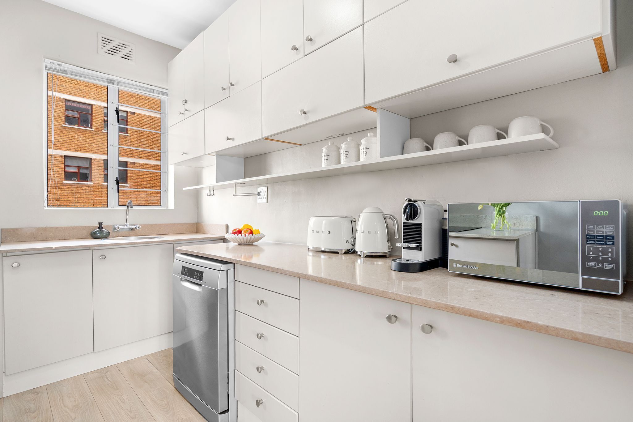 Una cocina moderna con armarios blancos, lavavajillas, cafetera y microondas.
