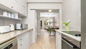 Una cucina moderna con mobili bianchi, lavastoviglie, fornello e zona pranzo con tavolo e sedie.