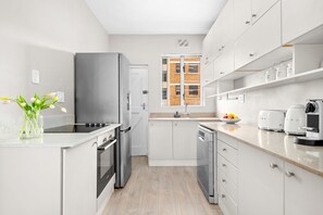 A modern kitchen with white cabinets, stainless steel appliances, and a view of a brick building through a window. - Fairmont 22 on Hof (Cape Town)