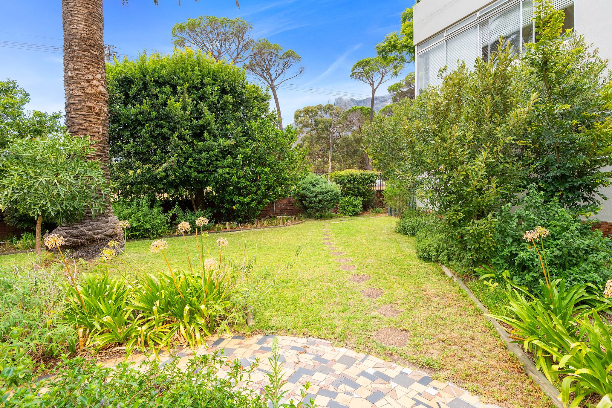 A well-maintained garden with a paved pathway, lush greenery, and a variety of plants.