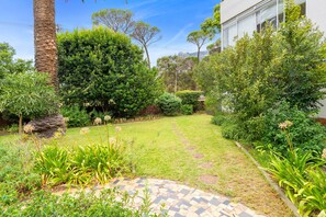 Un jardí ben cuidat amb un camí pavimentat, vegetació abundant i una varietat de plantes.