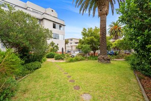 A well-maintained garden with a pathway, palm trees, and a building with balconies. - Fairmont 22 on Hof (Cape Town)